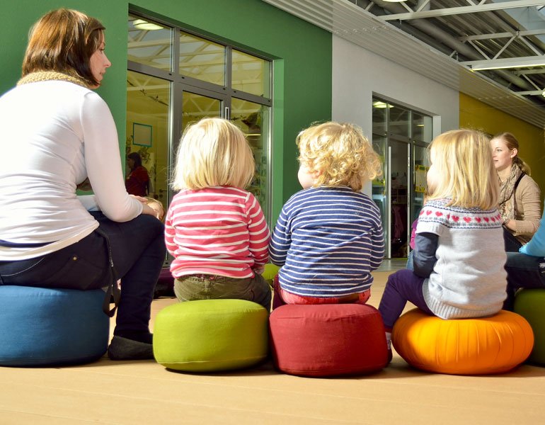 Erzieher und Kinder sitzen auf Bodenkissen im Sitzkreis